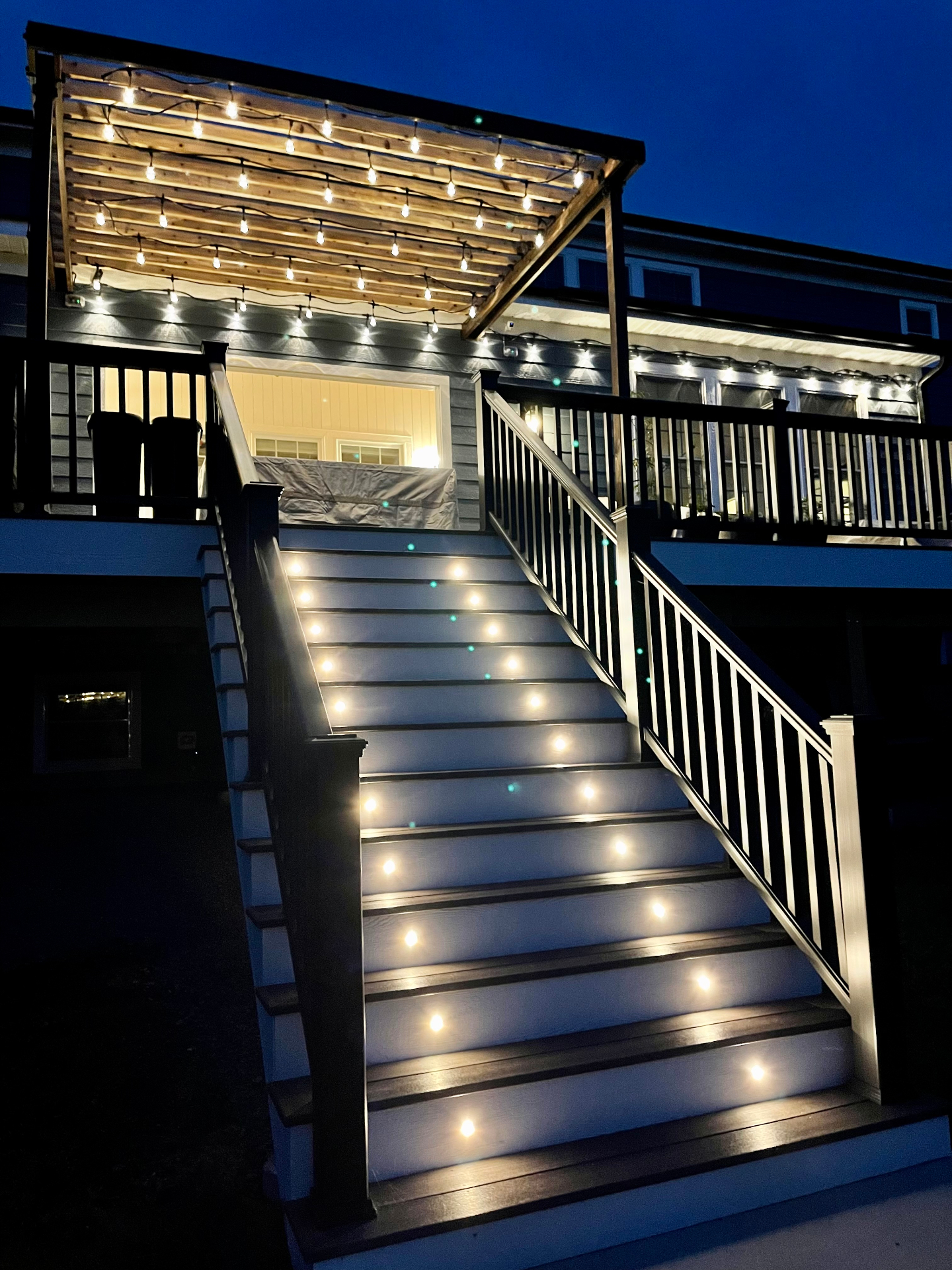 Custom deck with pergola, string lights, and illuminated stair risers by Streamline Renovates