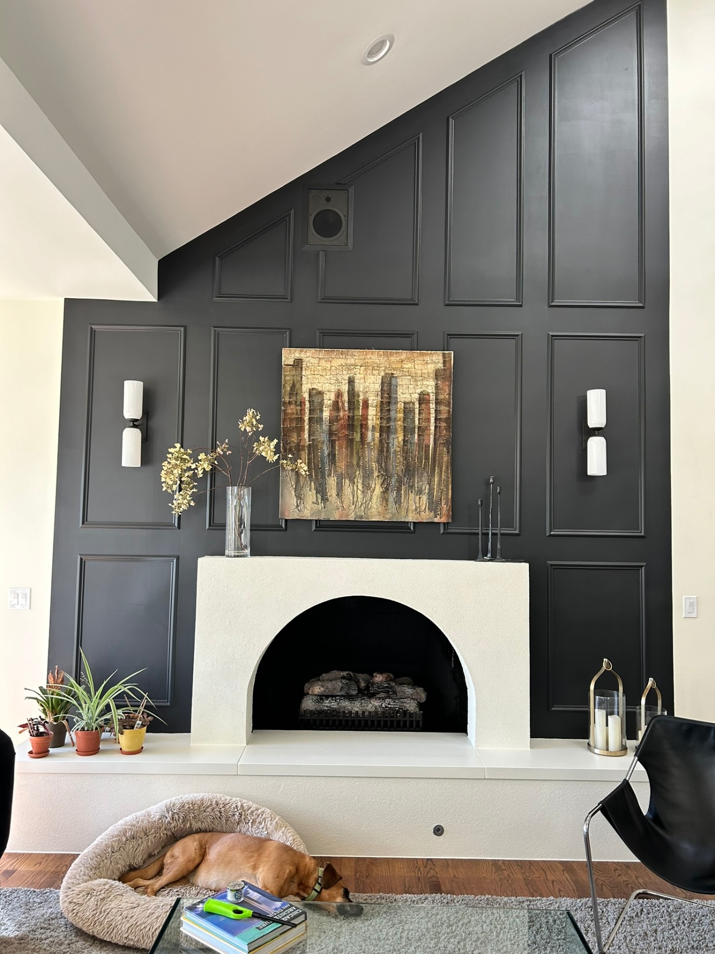 Modern living room with arched white fireplace and dark paneled accent wall by Streamline Renovates